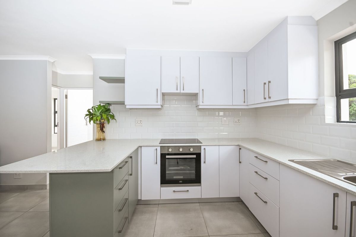 Modern kitchen featuring white cabinetry, stone countertops, subway tile backsplash, built-in oven, and hob, with a breakfast bar peninsula and tiled flooring.