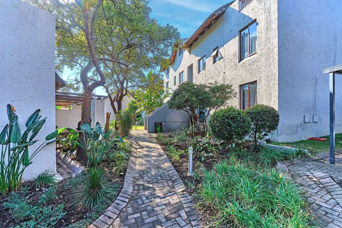 A view of the exterior rear garden area featuring a paved walkway, established landscaping, and the side elevation of the cluster property.