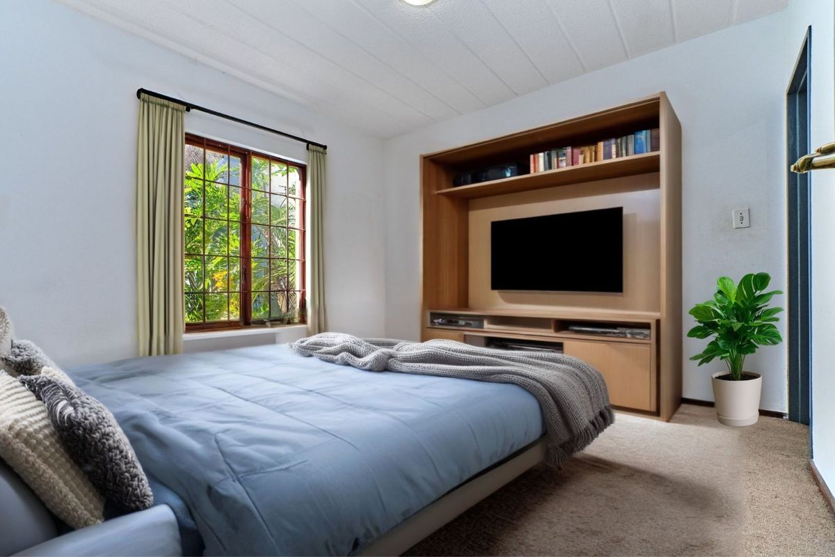 A bedroom featuring a built-in wooden media unit and a window with garden views.