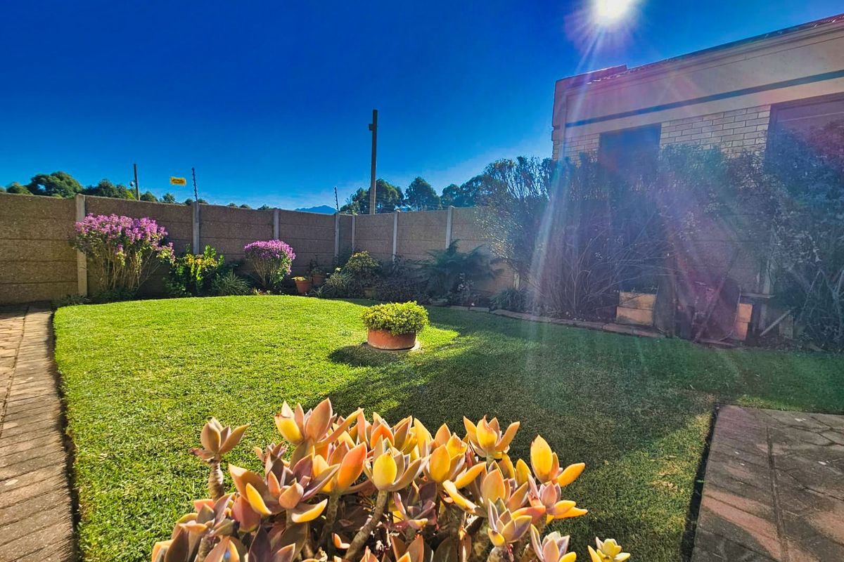 A well-maintained rear garden featuring a manicured lawn, paved pathways, and perimeter boundary walling.