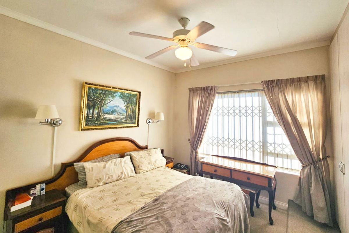 A well-maintained bedroom featuring a ceiling fan, built-in cupboards, and security bars on the window.
