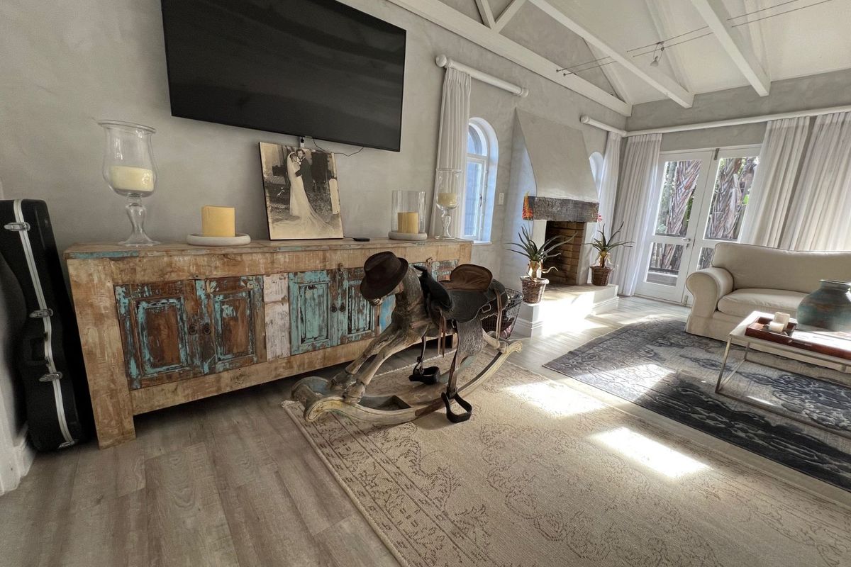 Spacious living room featuring a vaulted ceiling with exposed beams, a built-in fireplace with stone surround, and direct access to the garden via french doors.