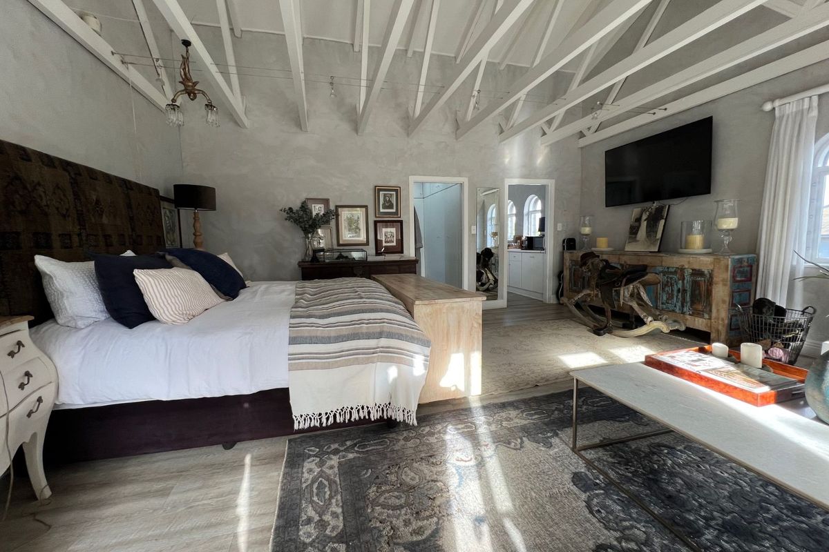 Spacious bedroom featuring high vaulted ceilings with exposed white timber rafters, neutral wall finishes, and durable laminate flooring.
