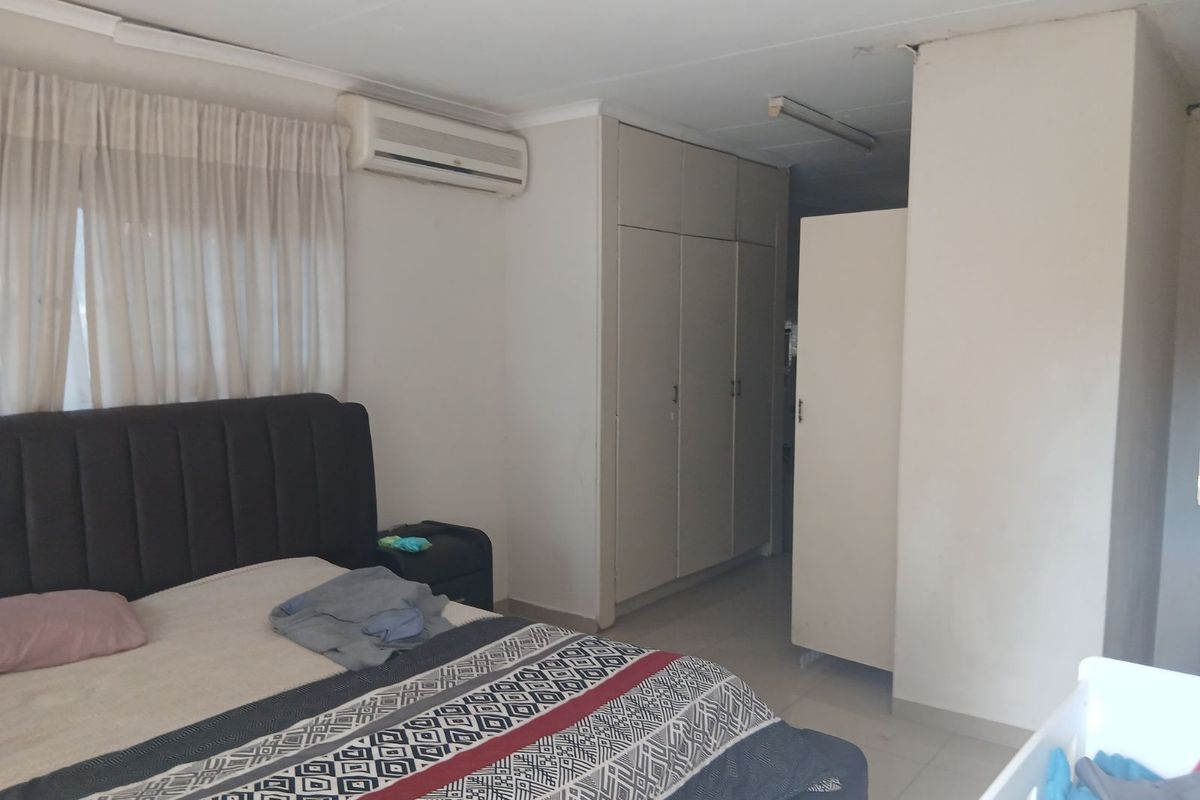 A bedroom featuring built-in cupboards, tiled flooring, and a wall-mounted air conditioning unit, requiring some cosmetic attention to the ceiling.