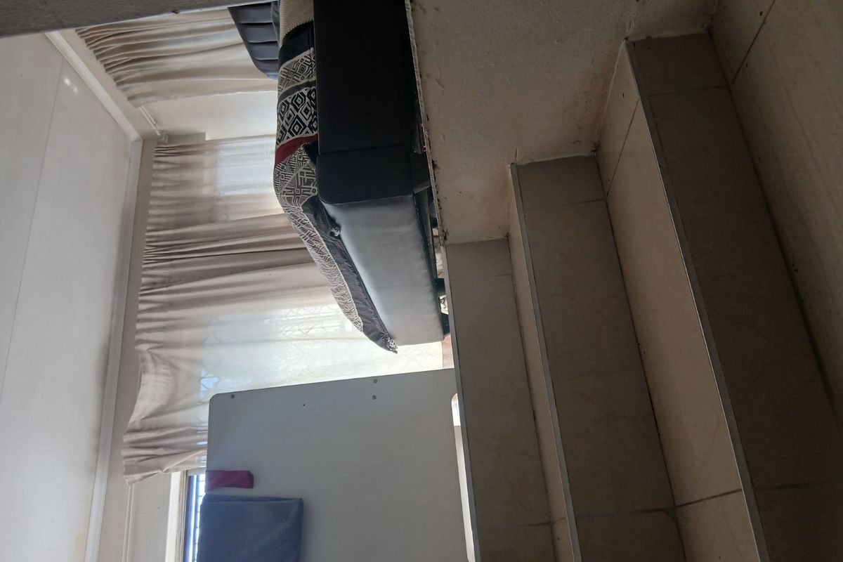 A living area featuring tiled flooring and window treatments, showing signs of wear and damage to the wall finishes.