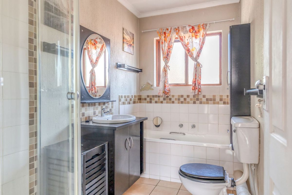 A functional bathroom featuring a built-in bathtub, separate glass-enclosed shower, vanity cabinet with basin, and tiled finishes.