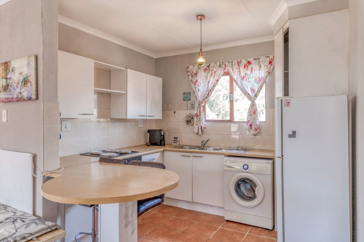 A functional kitchen featuring white cabinetry, tiled splashbacks, a built-in hob, and a dedicated space for a washing machine with an integrated breakfast nook.