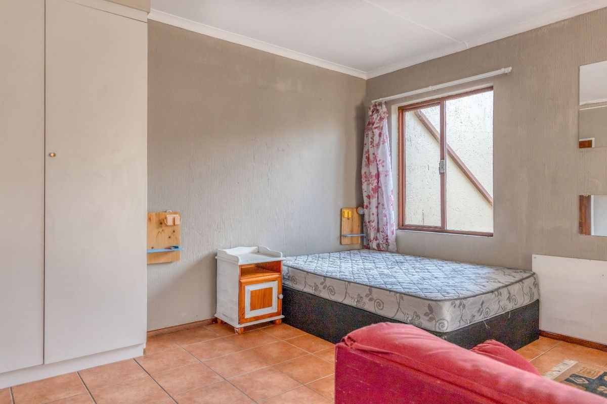 A bedroom featuring built-in cupboards, tiled flooring, and a window with natural light.