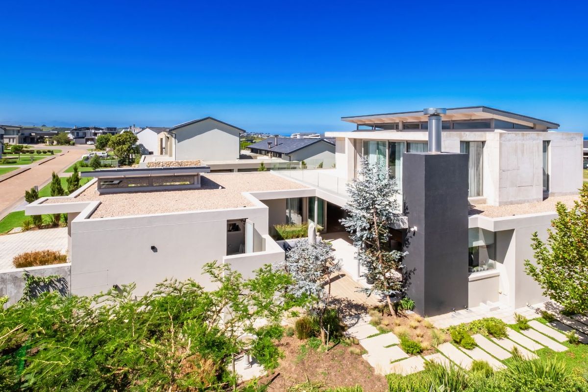 An elevated aerial view of a modern architectural house featuring a flat roof design, prominent chimney stack, and landscaped garden with paved pathways.