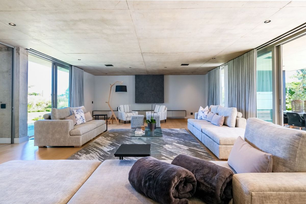 Spacious modern living area featuring a raw concrete ceiling, large sliding glass doors, and seamless indoor-outdoor flow to the patio.