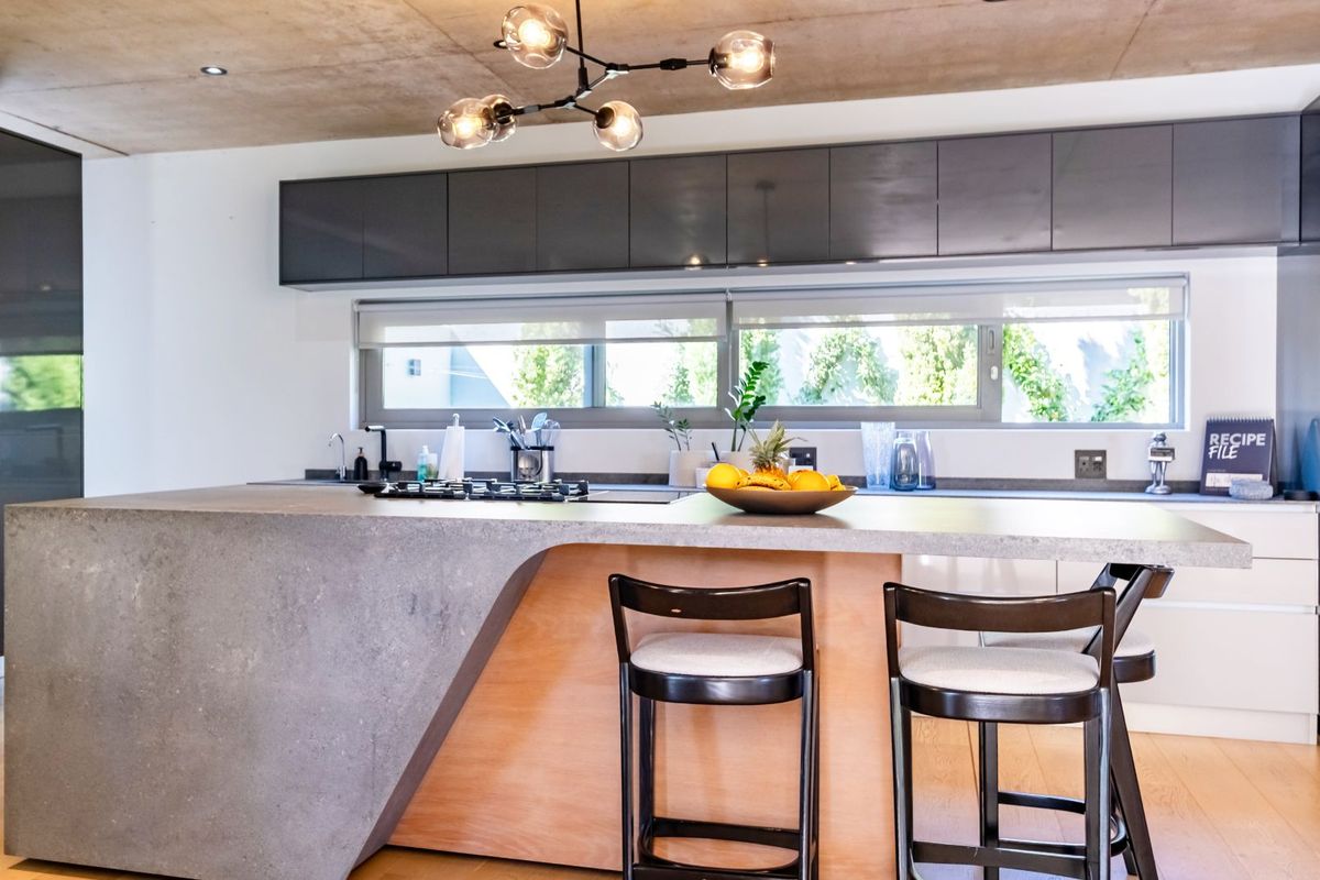 Modern kitchen featuring a large concrete island with integrated cooktop, sleek cabinetry, and a raw concrete ceiling finish.