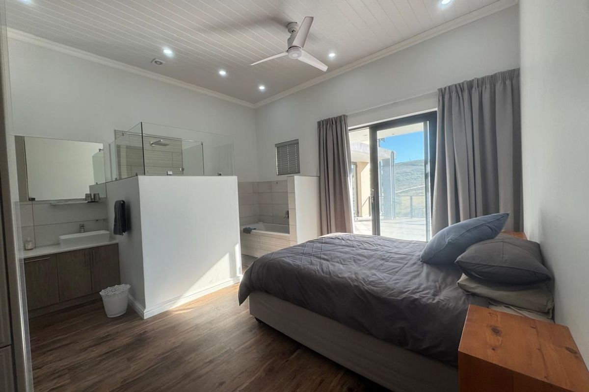 Spacious bedroom featuring an open-plan en-suite bathroom with a glass-enclosed shower, bathtub, vanity, and sliding door access to an outdoor patio area.