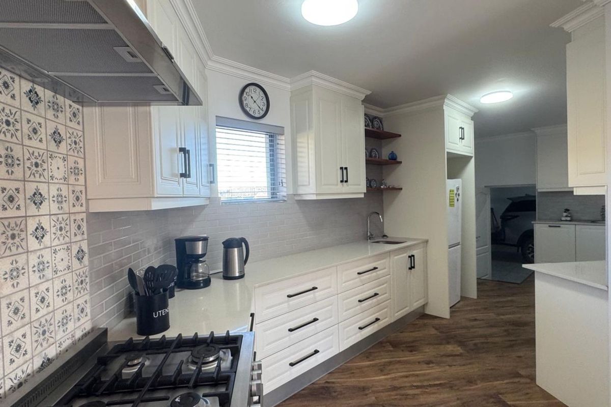 Modern kitchen featuring white cabinetry, stone countertops, subway tile backsplash, gas hob, extractor fan, and wood-look flooring.