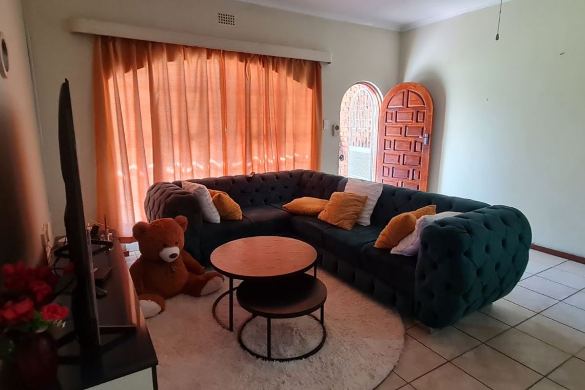 A living room area featuring tiled flooring, a large window with curtains, and a wooden entrance door.
