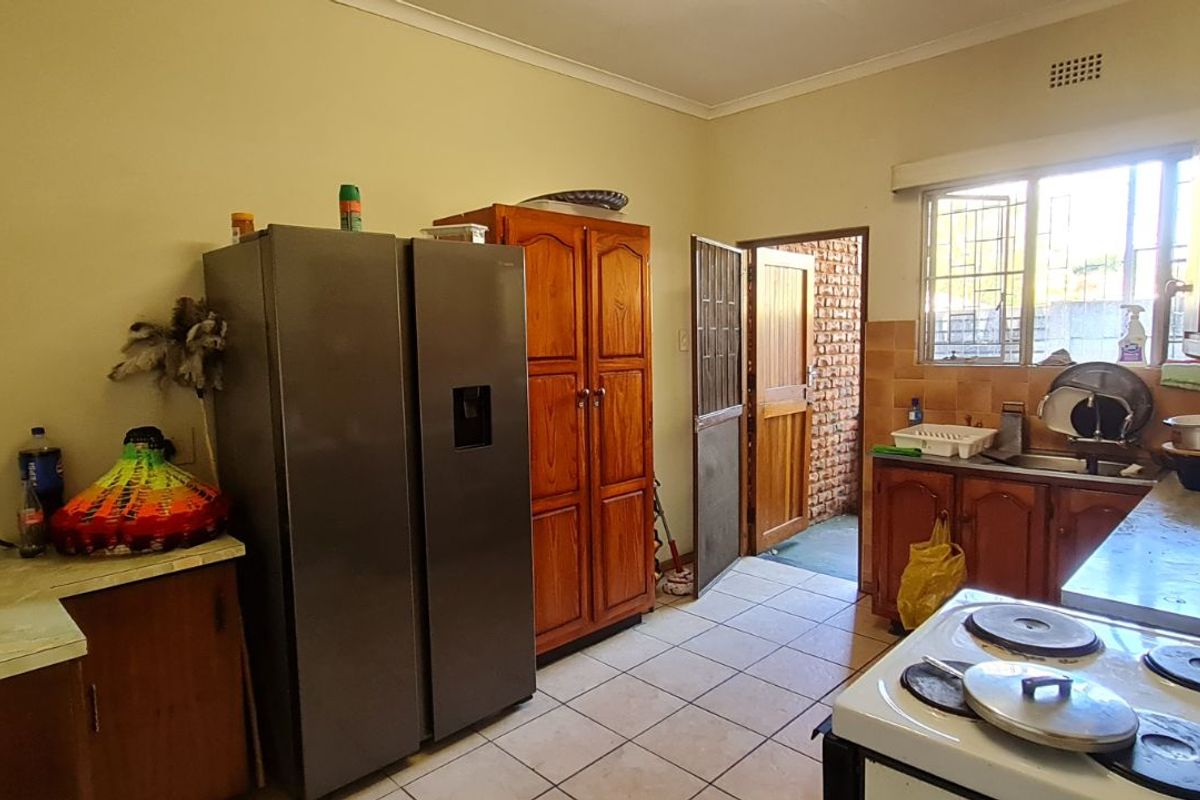 A functional kitchen featuring wooden cabinetry, tiled flooring, and a built-in stove, providing direct access to the exterior through a security door.