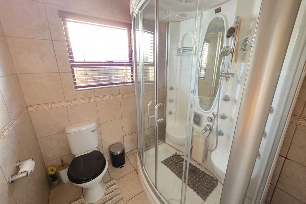 A functional bathroom featuring a corner multi-jet shower enclosure, ceramic wall and floor tiling, and a standard toilet.