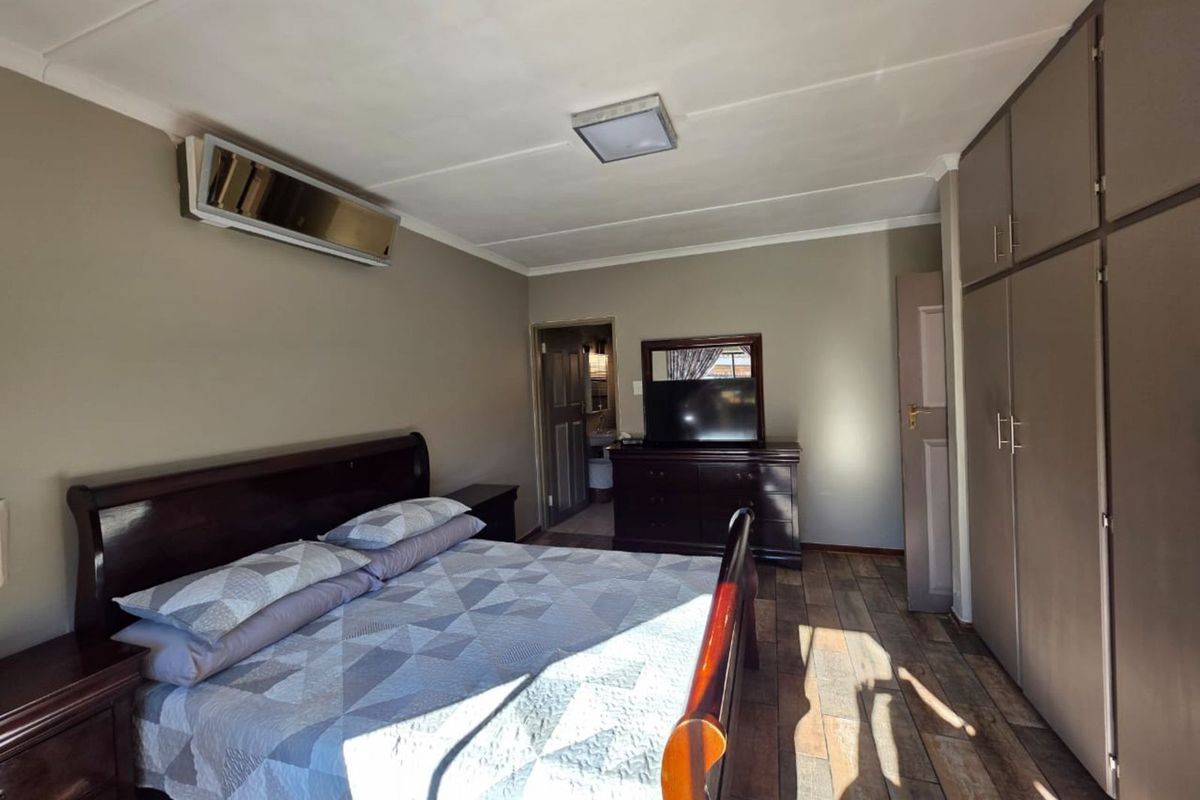 A bedroom featuring built-in cupboards, tiled flooring, and a wall-mounted air conditioning unit.