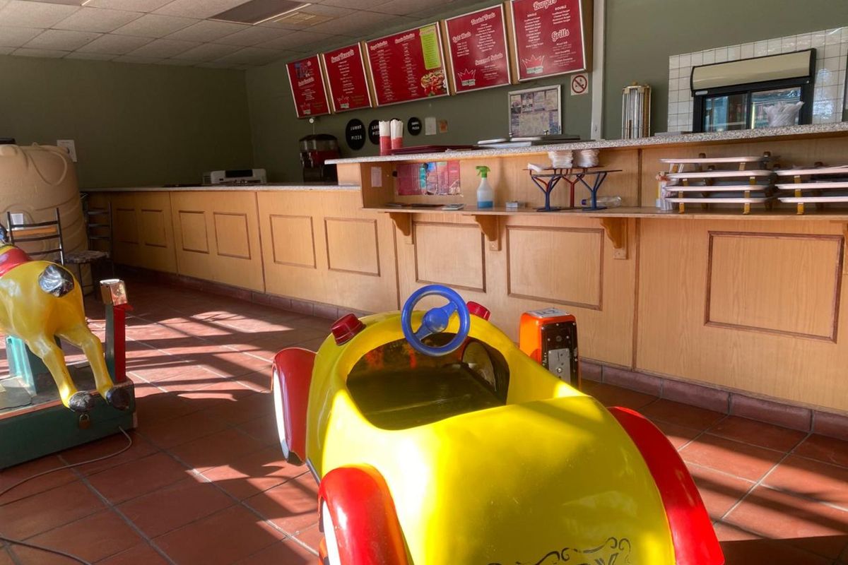 Retail service counter area featuring a long wooden service desk, tiled flooring, and menu boards, suitable for a food service or takeaway establishment.