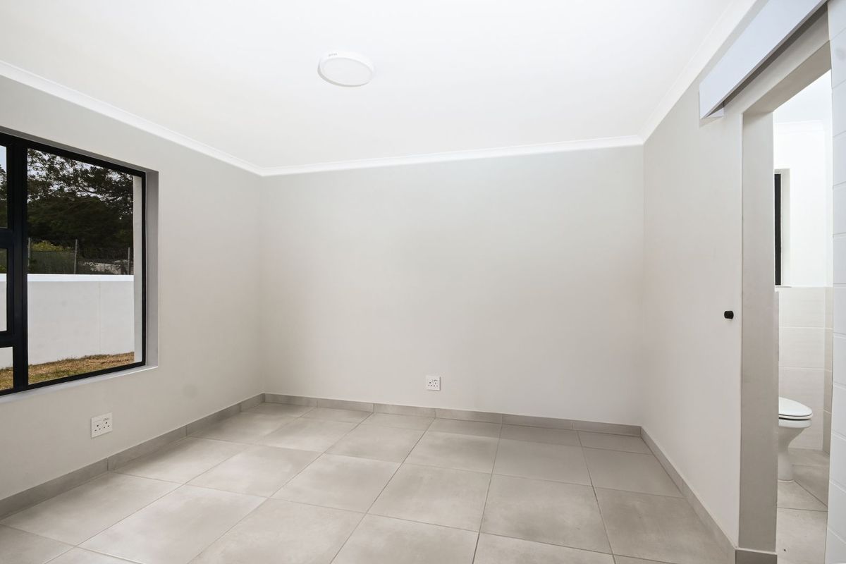 A bright, empty bedroom featuring neutral tiled flooring, modern aluminium-framed windows, and an adjoining en-suite bathroom.