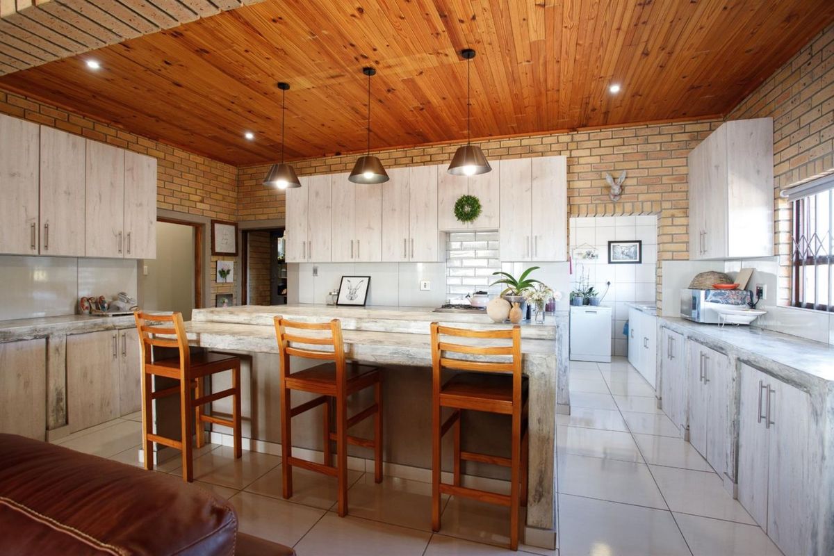Spacious kitchen featuring a large breakfast bar, light wood-look cabinetry, exposed brick walls, and a warm timber-paneled ceiling.