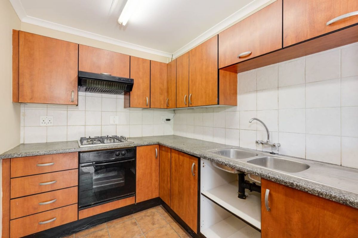 A functional kitchen featuring wood-look cabinetry, a built-in oven with gas hob, extractor fan, and a double stainless steel sink.