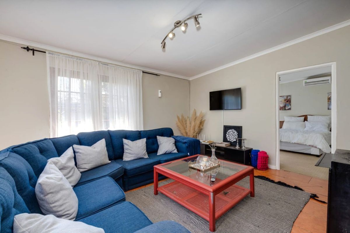 A comfortable living room featuring tiled flooring, track lighting, and a doorway leading to an adjacent bedroom equipped with a wall-mounted air conditioning unit.