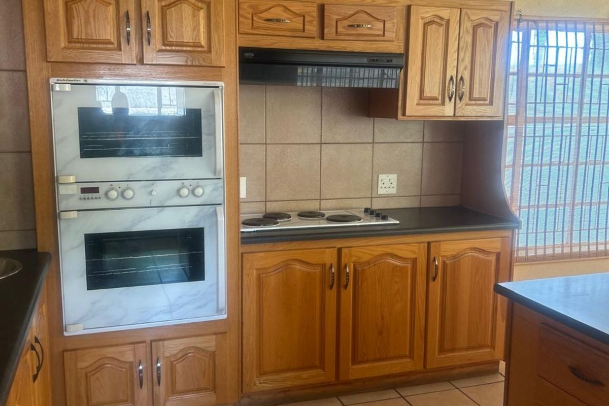 A functional kitchen featuring traditional timber cabinetry, built-in double oven, electric hob, extractor fan, and tiled flooring.