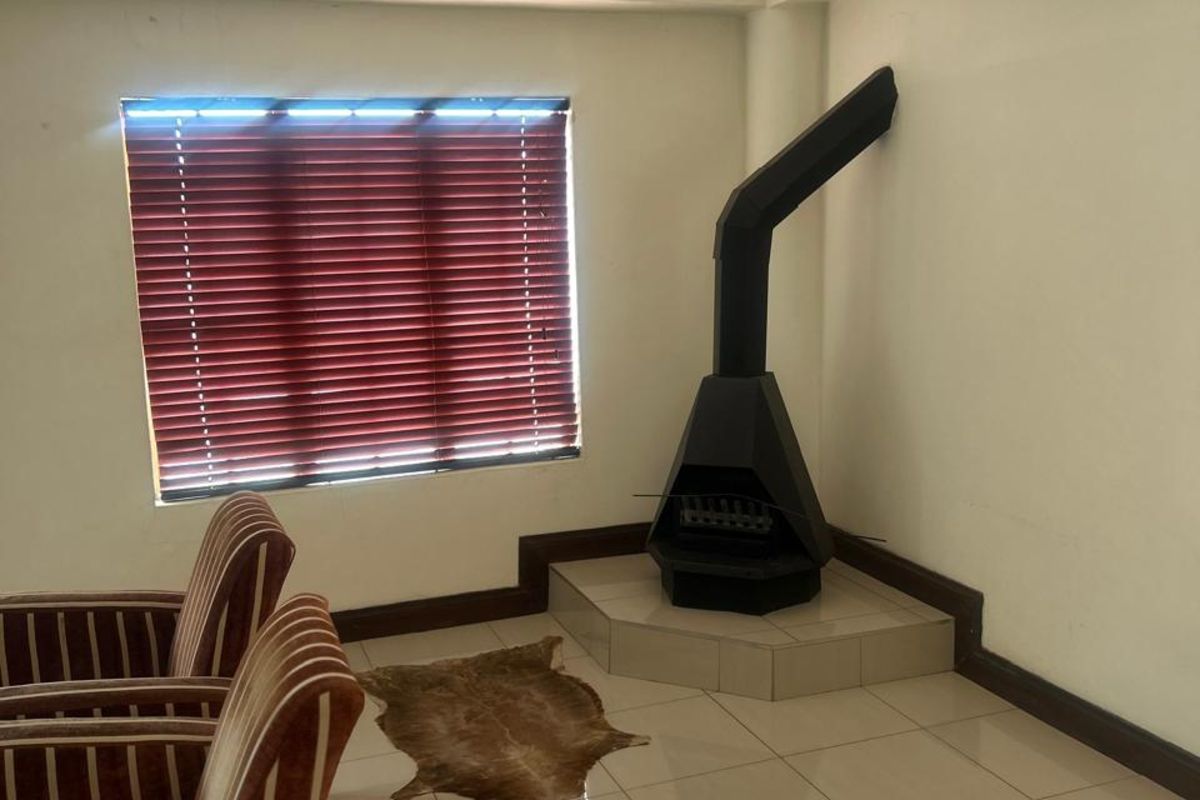 Living room featuring tiled flooring, a built-in corner fireplace with a metal flue, and window blinds.