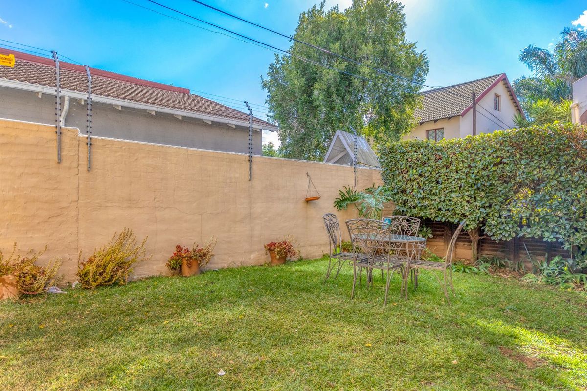 A private rear garden area featuring a lawn, established hedge, and a high boundary wall equipped with electric fencing for added security.