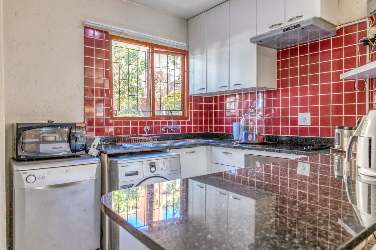A functional kitchen featuring granite countertops, white cabinetry, a red tiled backsplash, and integrated space for laundry appliances.