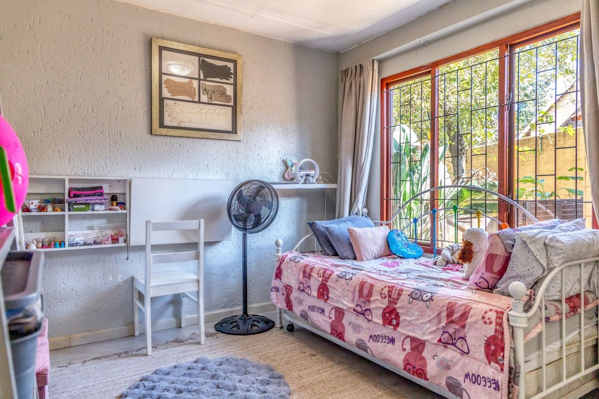 A bedroom featuring textured walls, a large window with security bars, and a built-in wall-mounted shelving unit.