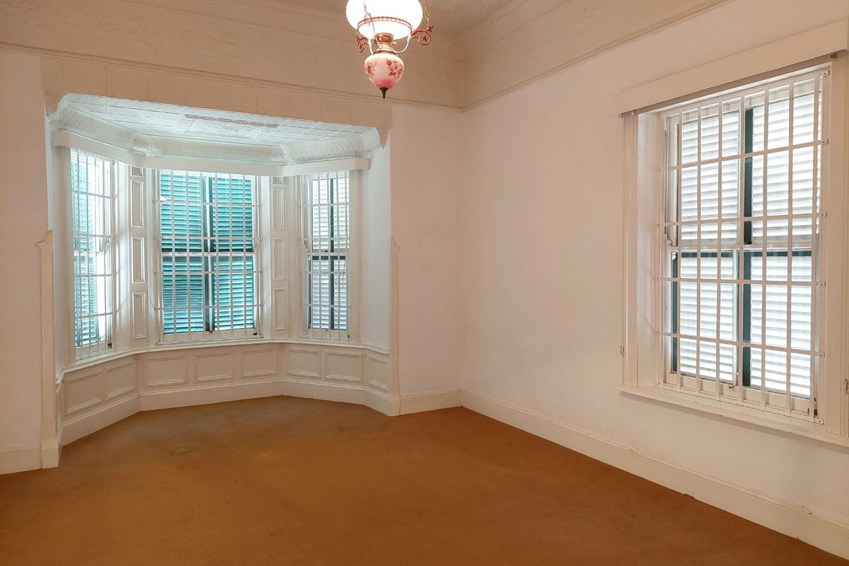 A bright, empty living room featuring a classic bay window, decorative ceiling molding, and secure window bars.