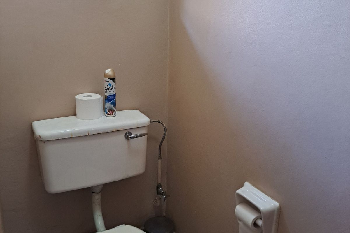 A compact bathroom featuring a standard toilet, tiled flooring, and a security-grilled window.