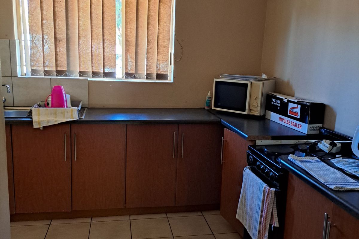 A functional kitchen featuring wood-finish cabinetry, dark laminate countertops, tiled flooring, and a built-in stove with an integrated sink area.