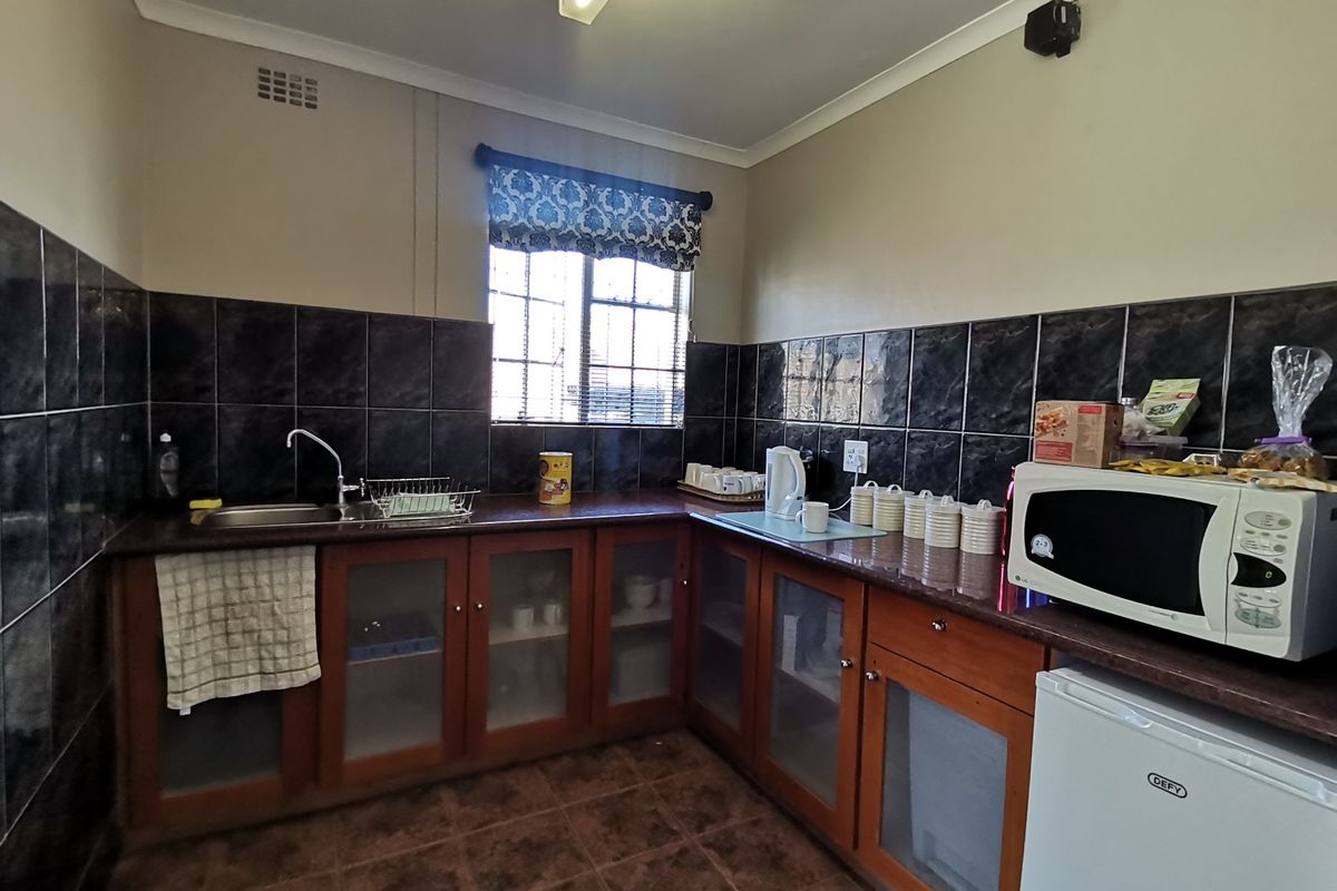A functional kitchen area featuring dark tiled splashbacks, wooden cabinetry with glass inserts, and a stainless steel sink.