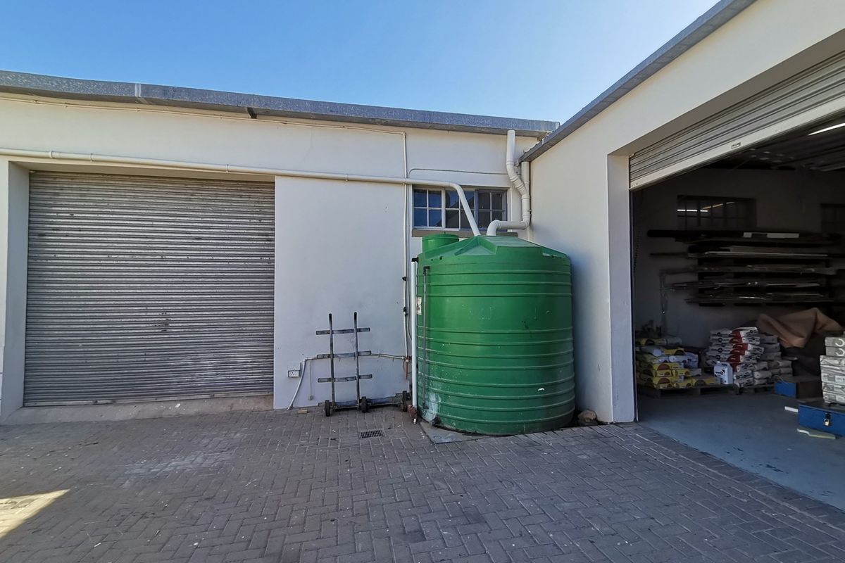 Exterior view of an industrial property featuring a roller shutter door, a large water storage tank, and paved access area.