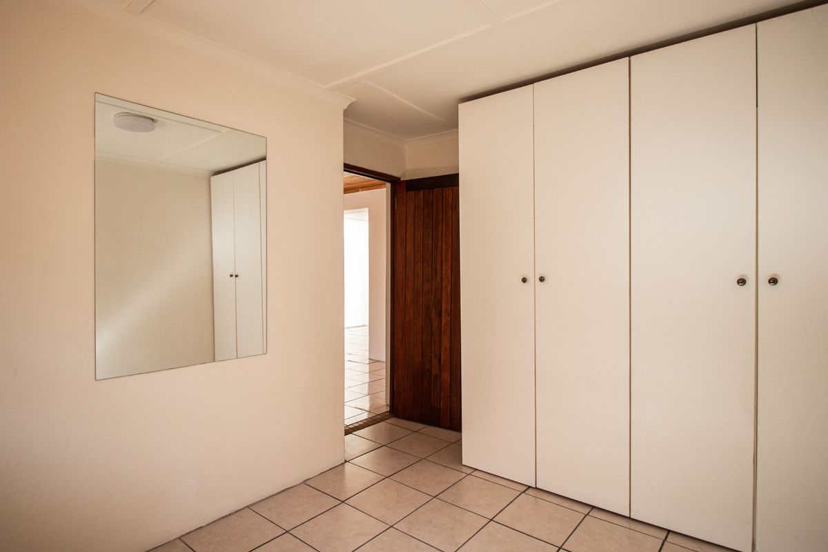 A bedroom featuring built-in white cabinetry, tiled flooring, and a wall-mounted mirror, leading to an adjacent room through a wooden door.