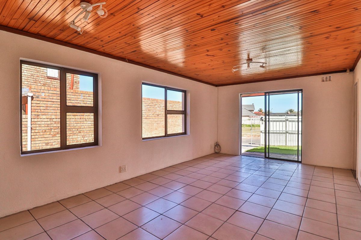 An empty living room featuring tiled flooring, a timber-clad ceiling, and sliding glass doors providing access to the exterior.