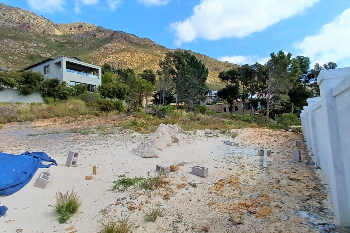 A vacant residential plot featuring a perimeter boundary wall, set against a scenic mountain backdrop in a developed neighborhood.