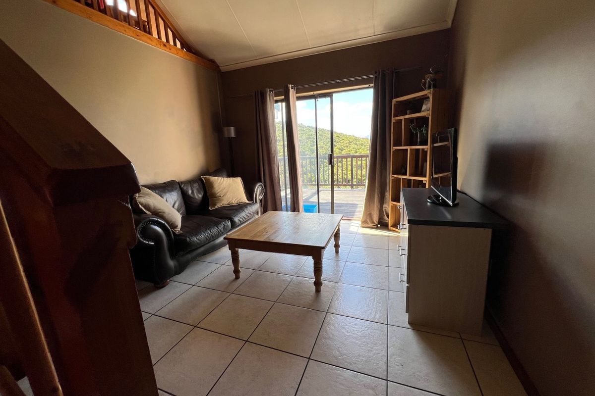 A living room featuring tiled flooring, a vaulted ceiling with timber detailing, and sliding glass doors providing access to an outdoor balcony.