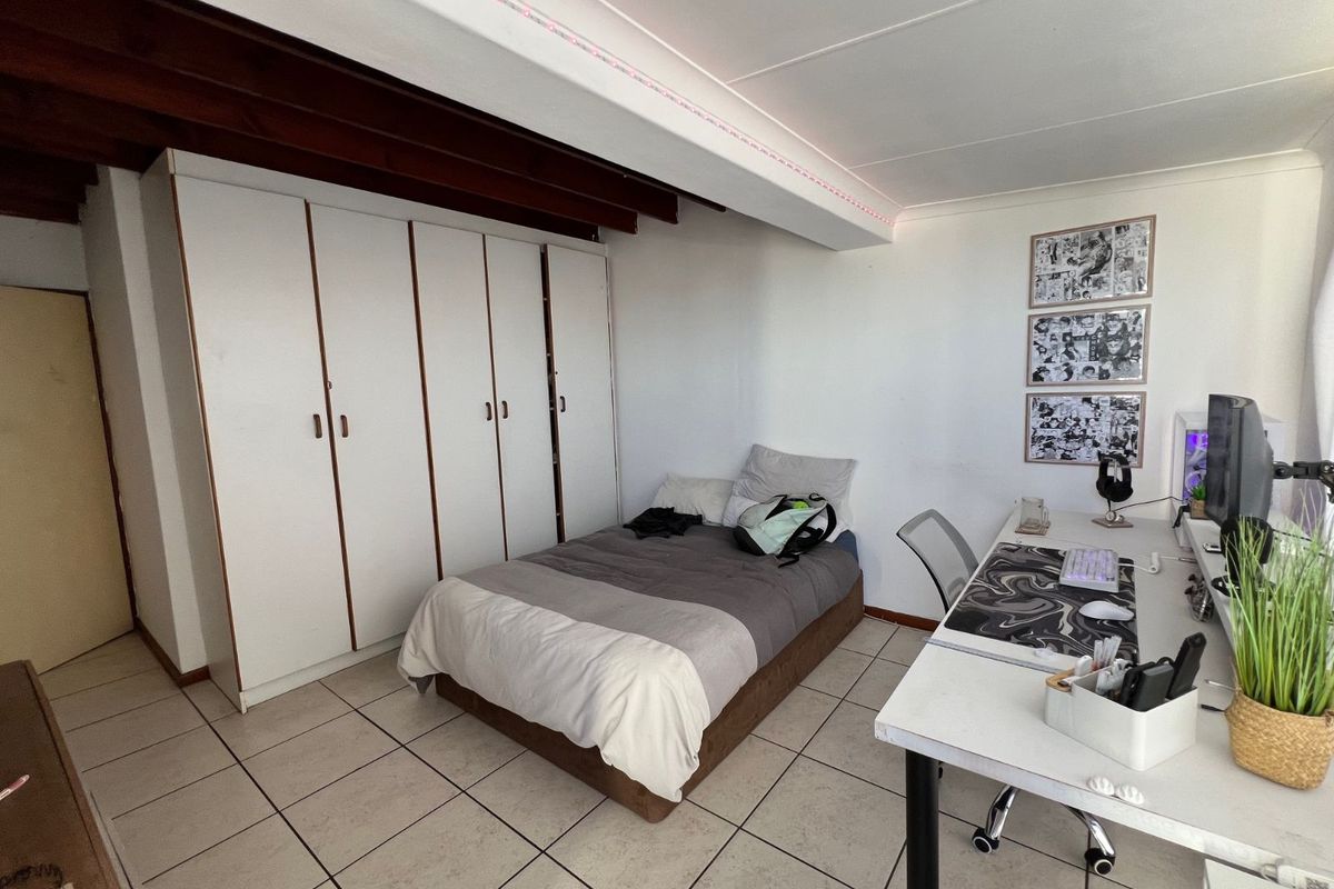 A bedroom featuring built-in wardrobes, tiled flooring, and exposed timber ceiling beams, providing a functional living space.