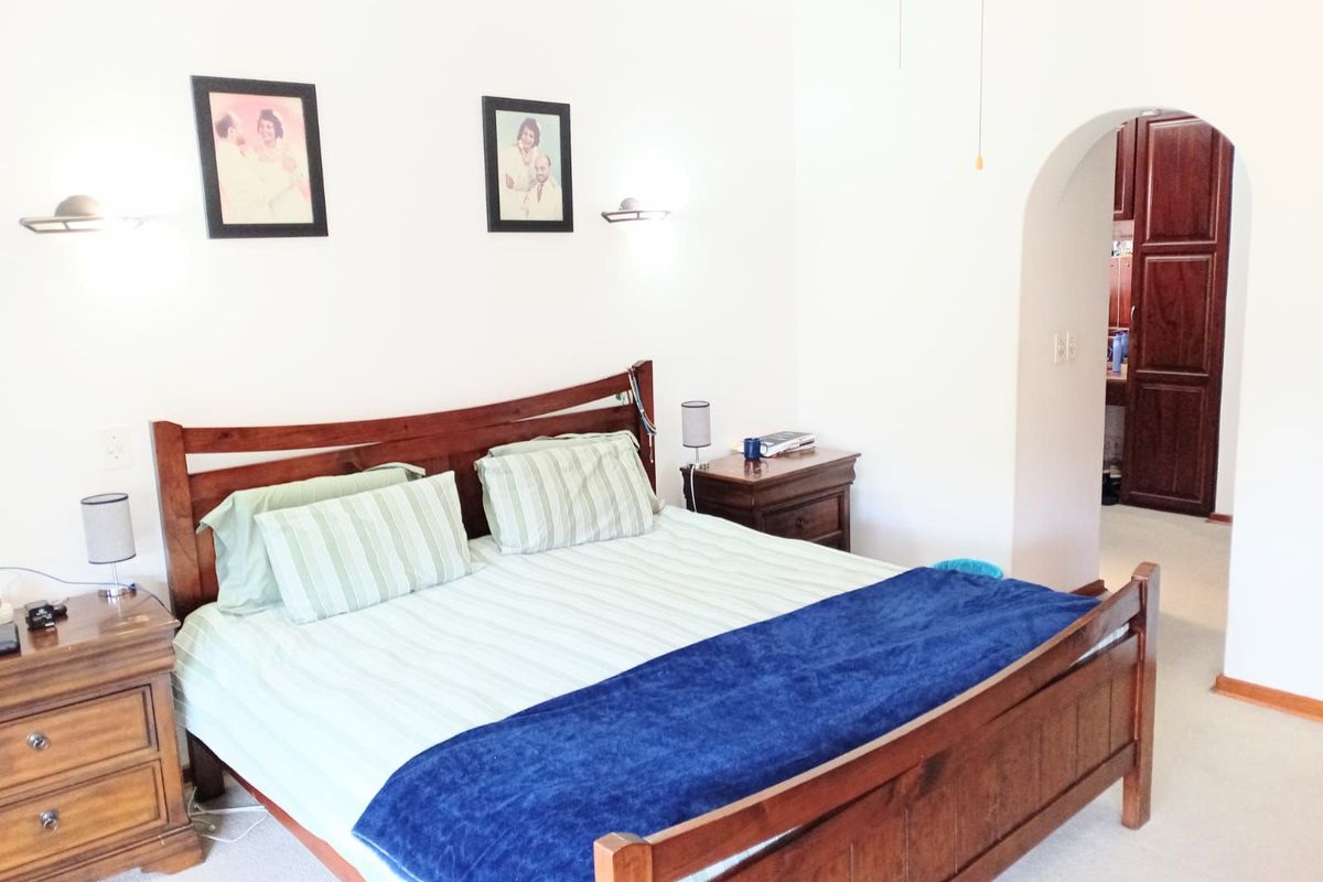 A bedroom featuring a classic arched doorway leading to an adjoining space, wall-mounted lighting fixtures, and neutral carpeting.