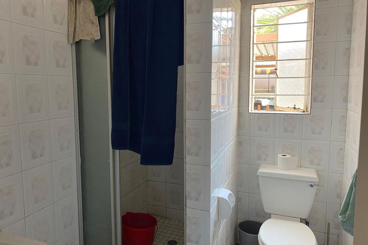 A compact bathroom featuring a shower enclosure, toilet, and tiled walls with a small window for natural ventilation.