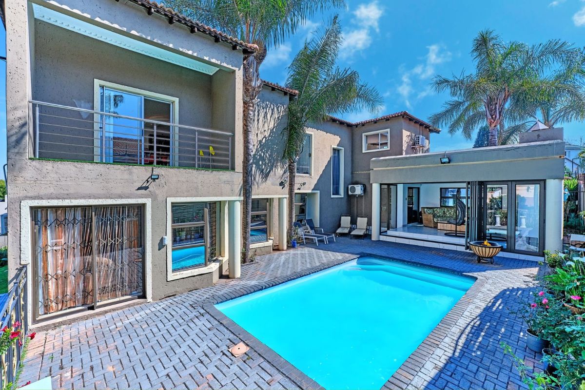 Rear exterior view featuring a swimming pool, paved patio area, upper-level balcony with stainless steel railing, and multi-story residential structure.