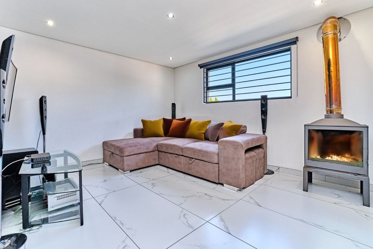 A modern living room featuring large format marble-look floor tiles, recessed ceiling lighting, a security-barred window, and a contemporary freestanding wood-burning fireplace.