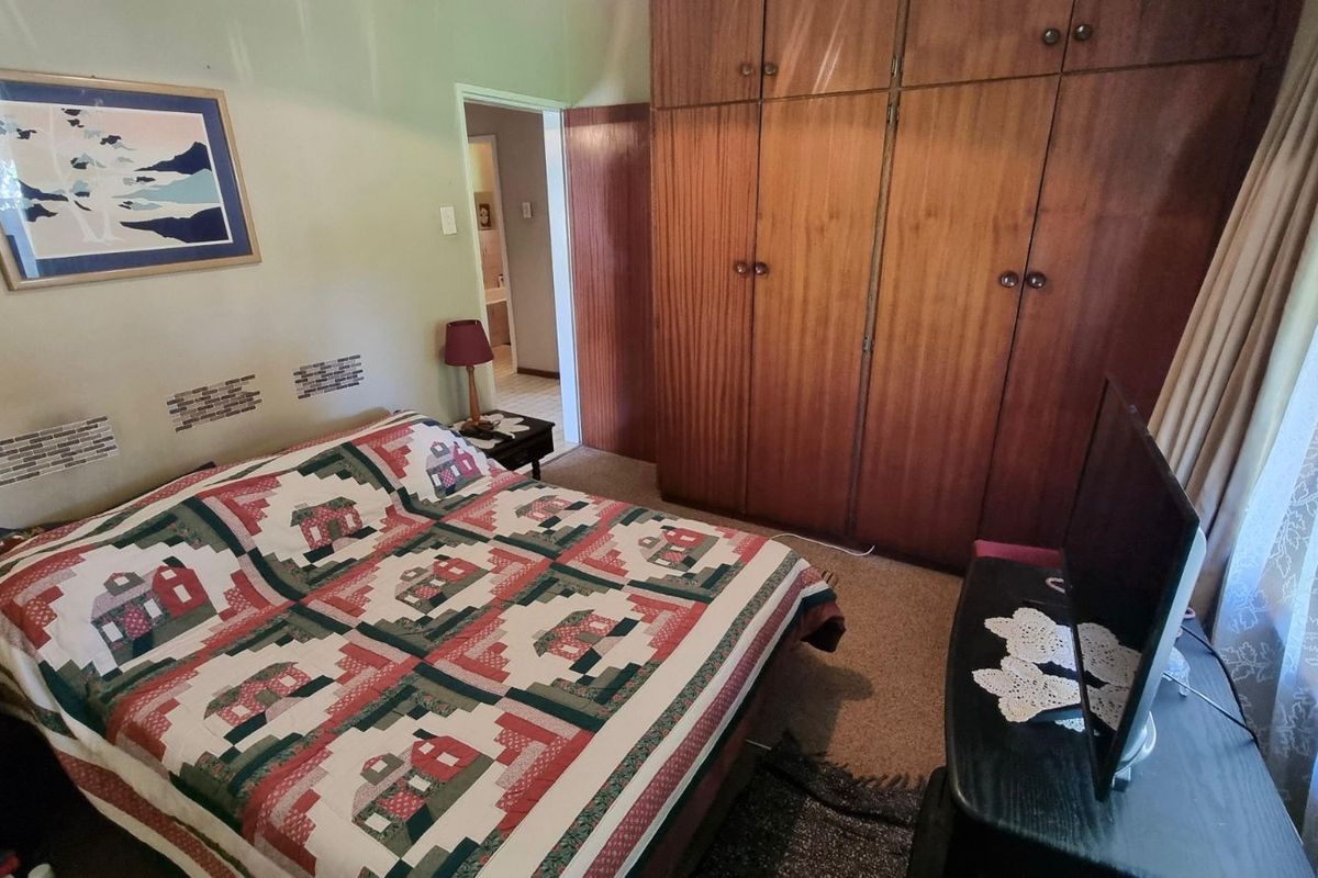 A bedroom featuring built-in wooden cupboards and carpeted flooring, with an adjacent doorway leading to an en-suite bathroom.
