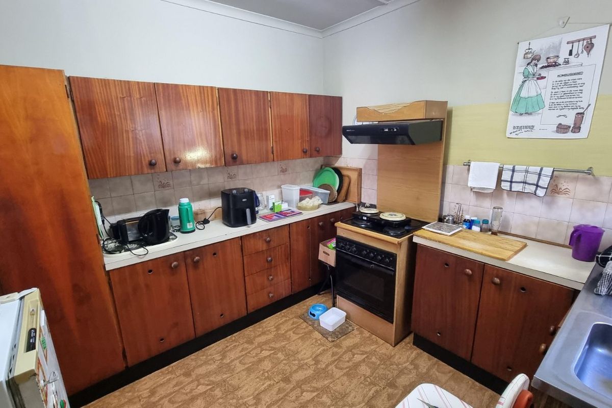 A dated kitchen featuring original wood cabinetry, a built-in oven with extractor fan, and tiled backsplash, offering potential for a modern renovation.