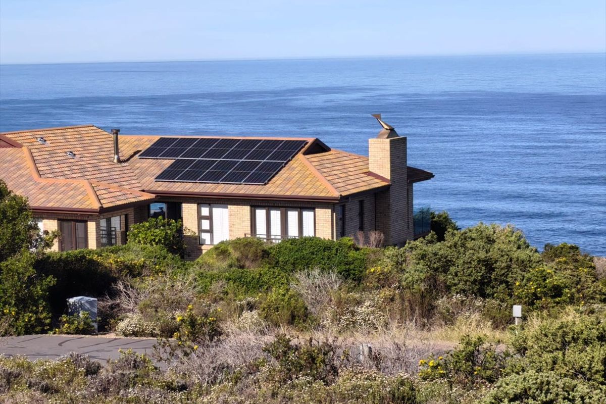 Elevated view of a coastal residence featuring a tiled roof, solar panel installation, and a prominent brick chimney overlooking the ocean.