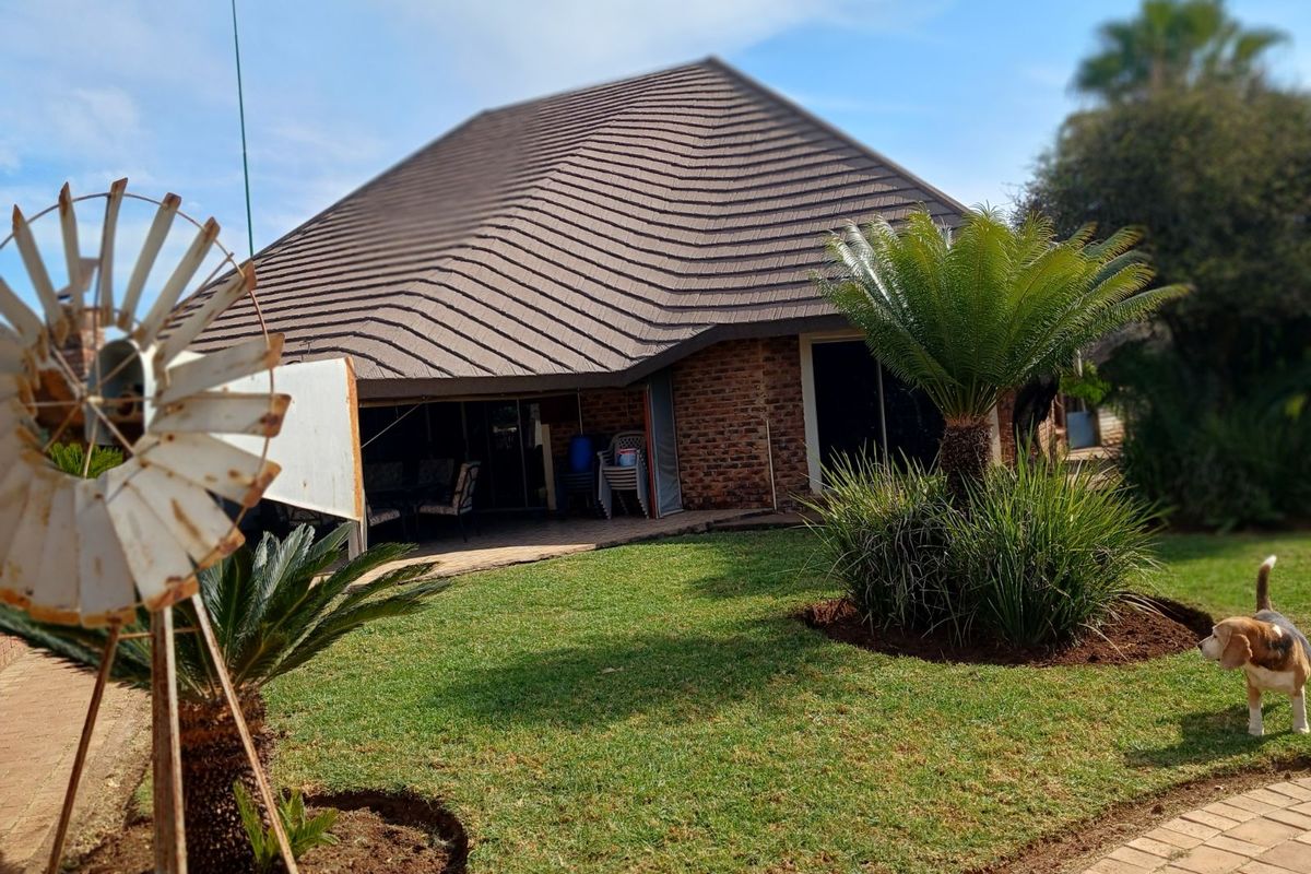 Rear view of a farm-style residence featuring a large tiled roof, brick facade, and a covered patio area overlooking a landscaped garden.