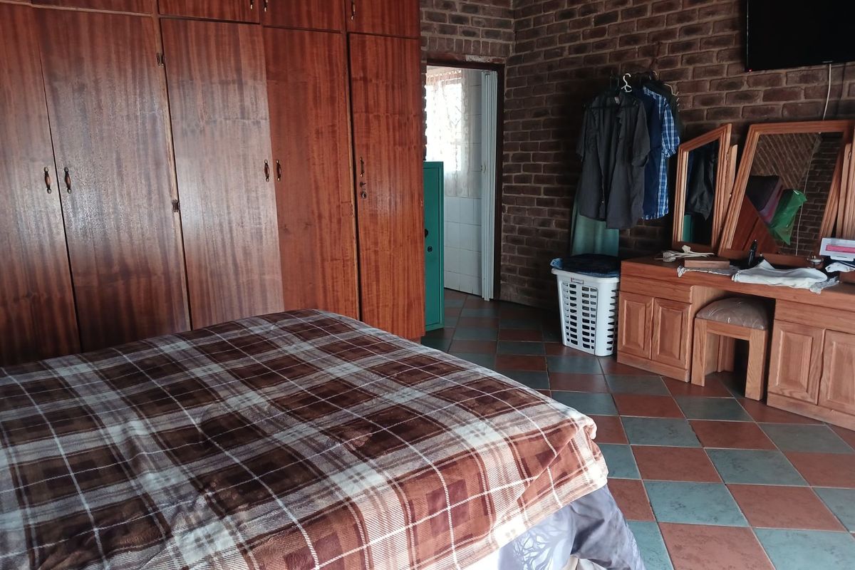 A rustic bedroom featuring exposed brick walls, built-in wooden wardrobes, and tiled flooring, with an adjoining doorway leading to an adjacent room.